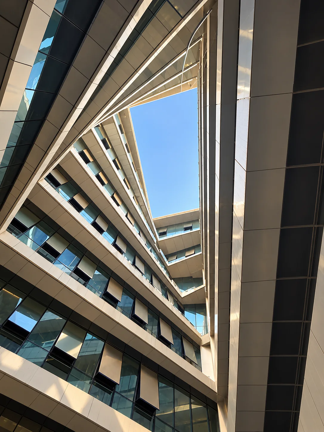 Upward view through iTower’s geometric atrium toward a clear blue sky